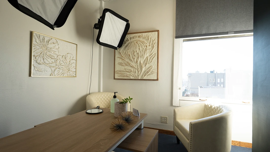 A bright consultation room with cream-colored tufted chairs, professional photography lighting, and large windows overlooking the city.