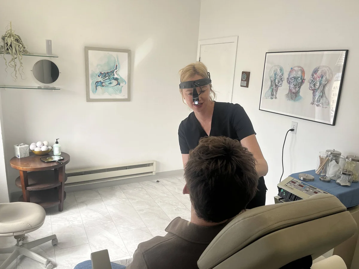 r. Noud uses a surgical headlamp to perform a detailed facial examination for a patient seated in a clinical treatment chair.