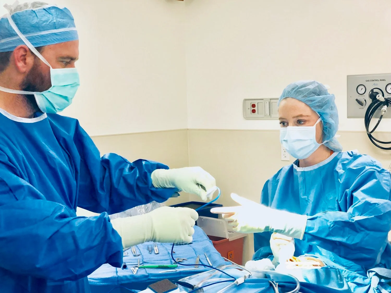 Dr. Noud in sterile blue scrubs and a mask, working with a surgical assistant to prepare instruments during a procedure.