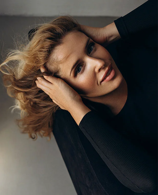 An artistic, high-angle shot of a woman with blonde hair, looking upward with a bright, open expression that highlights a smooth forehead and lifted brow area.