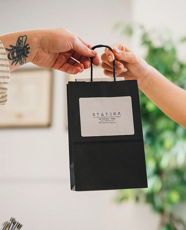 A close-up of a patient’s hand receiving a black shopping bag from the Statera Cosmetic and Reconstructive Surgery clinic, representing their personalized skincare services.
